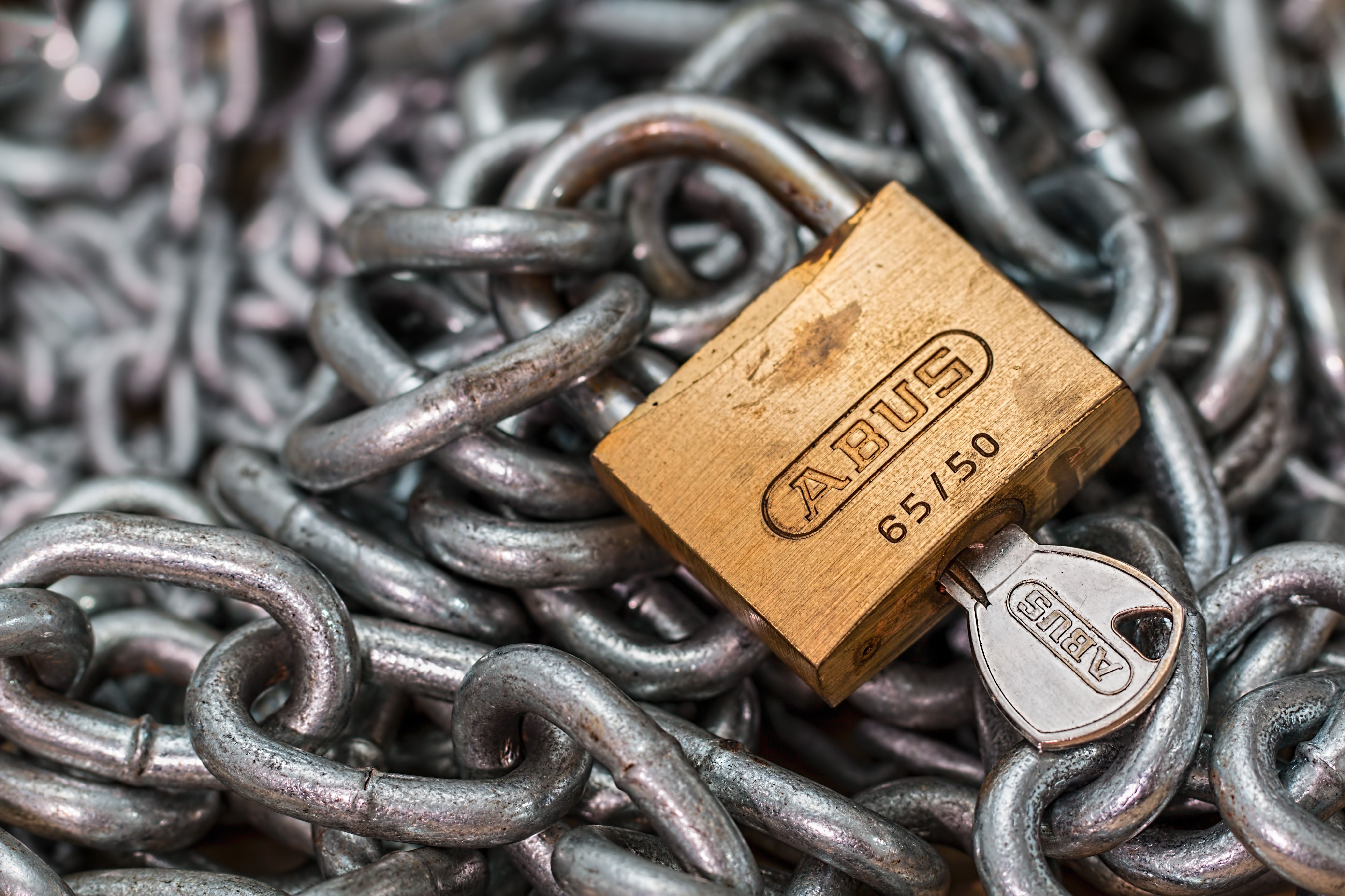 Cadenas doré avec sa clé, posé sur une chaîne en métal.